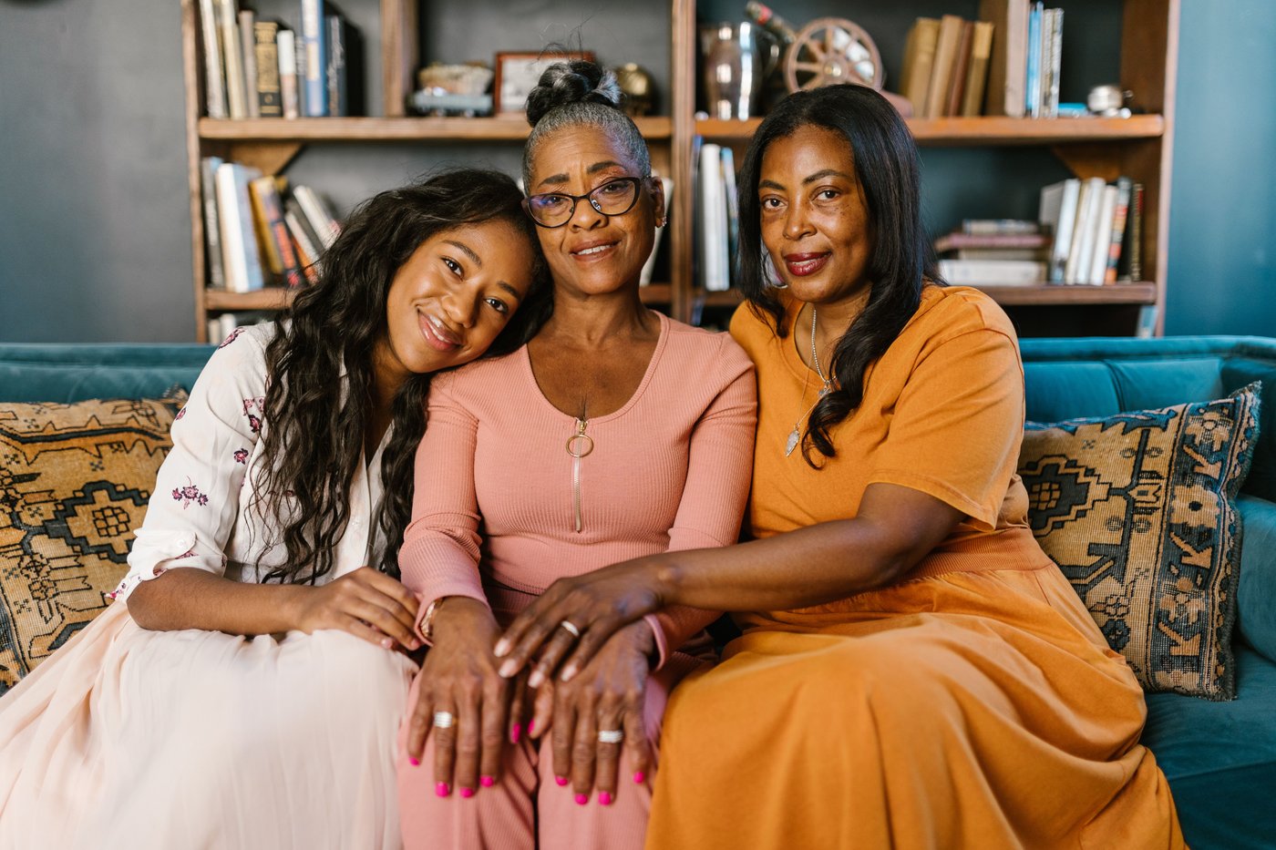 A woman seated between her two adult daughters, their hands resting together in her lap