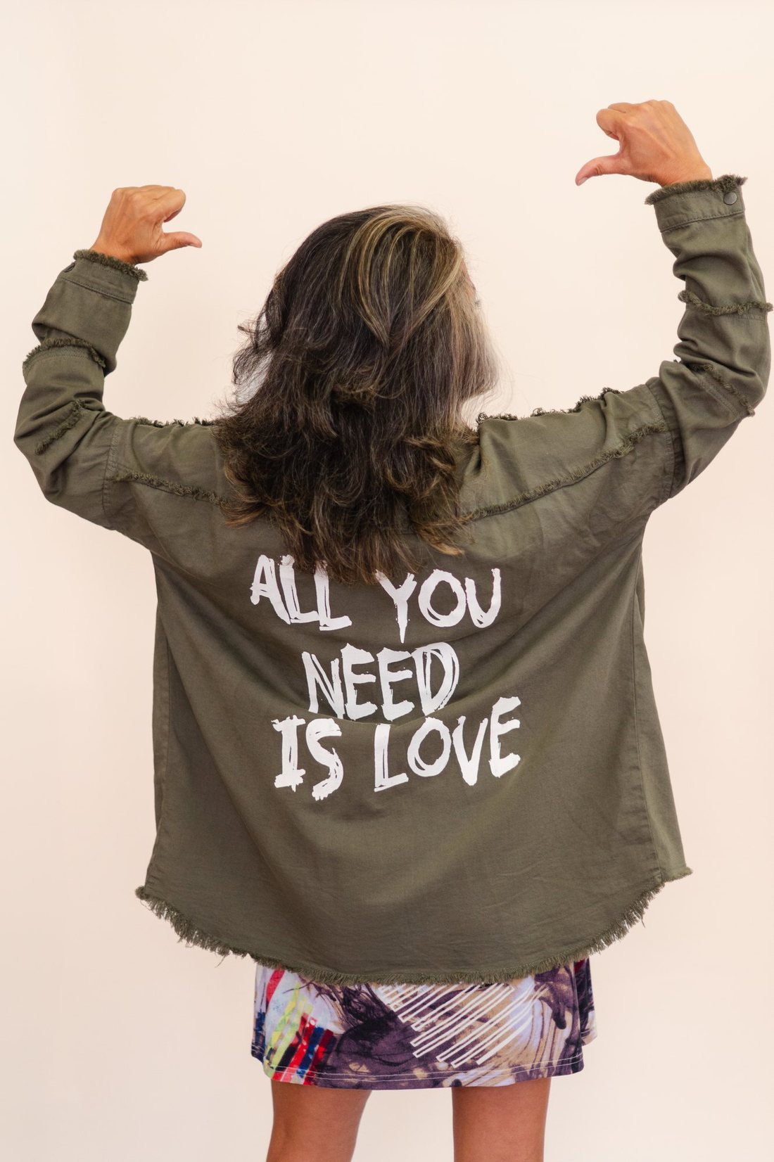 Monique Alem&aacute;n from behind, arms raised, in a jacket reading All You Need Is Love